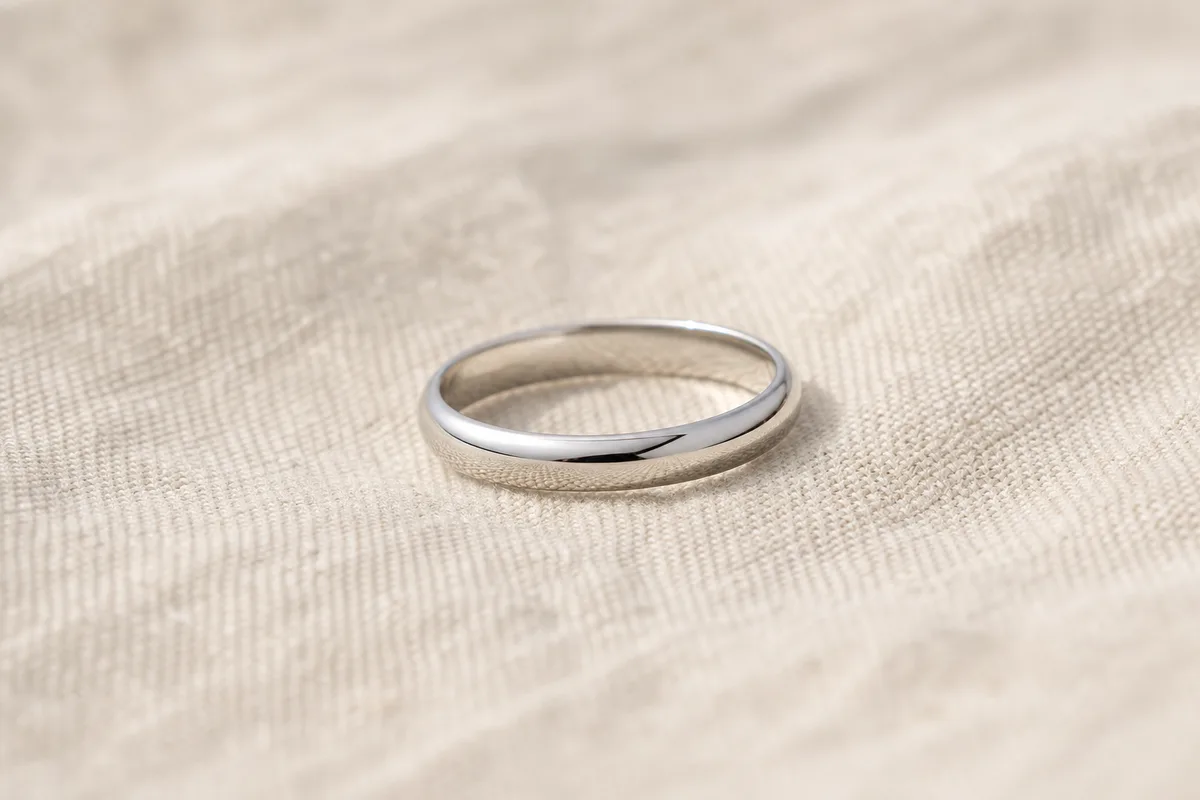 Bague en or blanc posée sur un tissu de lin clair, lumière naturelle rasante